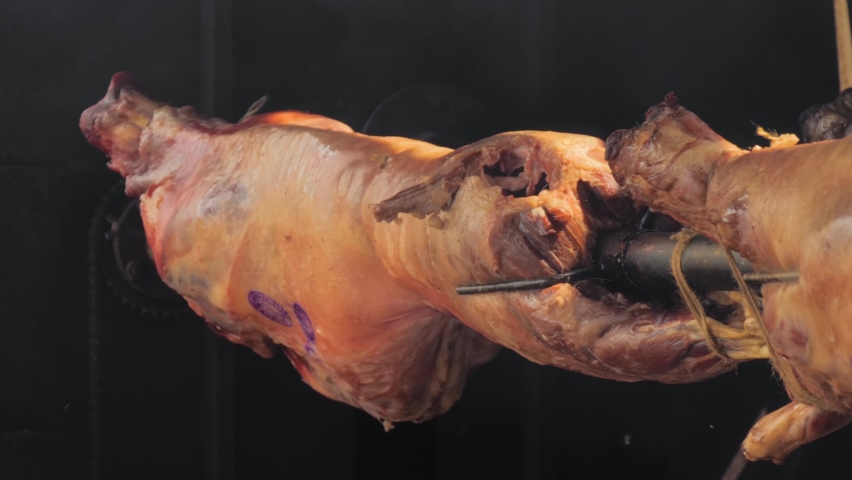 Process of cooking roasted whole ram carcasses on spit at summer outdoor food festival, market: close up. Professional cooking, preparation, cookery, gastronomy and street food concept