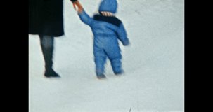 Funny little child falls on slippery snow in winter, mother helps to get up. Small kid in blue jacket walks with mother in snowy park. Happy family. Vintage color film. Family archive. Retro 1980s