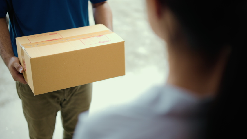 Close up parcel in hand of blue uniform delivery man to customer front of the house with good service from shopping online. Courier man delivering a cardboard box postal package to destination. Royalty-Free Stock Footage #1090939535