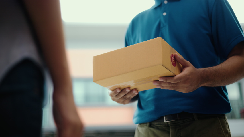 Close up parcel in hand of blue uniform delivery man to customer front of the house with good service from shopping online. Courier man delivering a cardboard box postal package to destination. Royalty-Free Stock Footage #1090939553