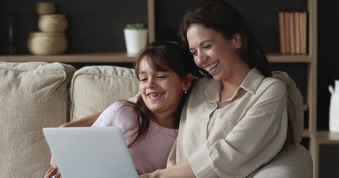 Young mom her little daughter rest on sofa with laptop, watch cartoons and movie through digital streaming on-line services, enjoy weekend at home use modern tech. Do e-shopping, make order feel happy