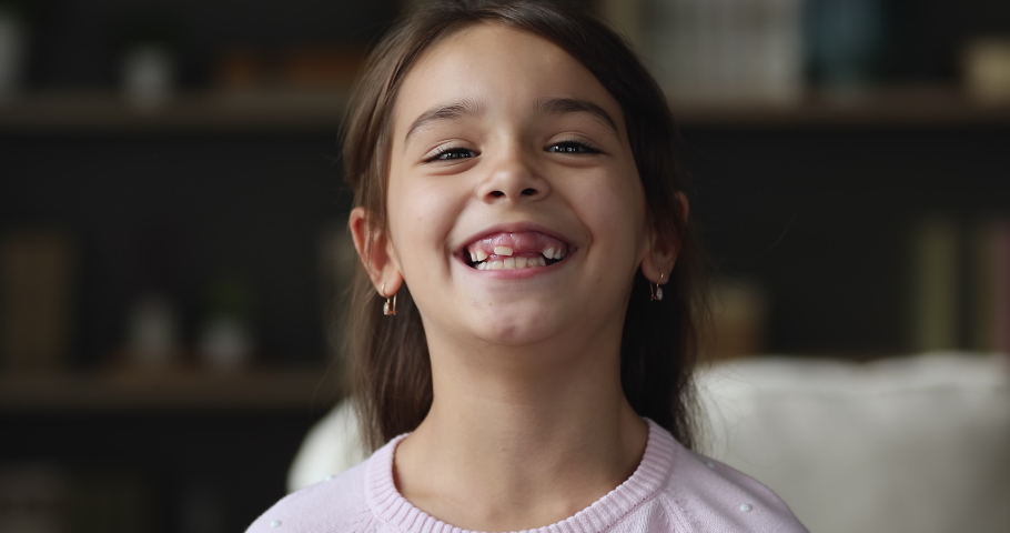Close up head shot pretty brown haired brunette little girl pose alone indoor staring at camera having wide smile, revealing erupted teeth. Candid kid, beautiful child portrait, generation Z concept | Shutterstock HD Video #1090941675