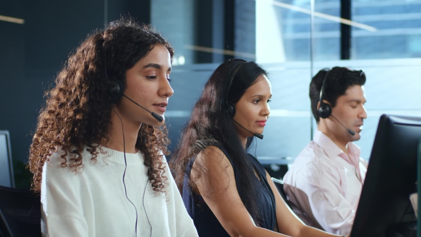 Young modern smiling Indian Asian male and female or mixed gender busy call center employees wearing headsets or headphones interacting with clients in corporate office. Customer care support concept Royalty-Free Stock Footage #1090942927