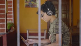 A young Indian Asian male boy or kid student wearing headphones and eyeglasses studying in online group video call class activity using a laptop. remote school, distance education, technology concept