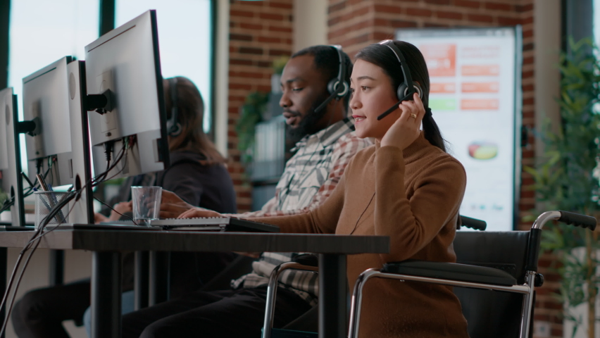Young woman working at customer assistance service, using microphone on headphones. Female worker talking to clients at call center, helping with remote telemarketing problems. Handheld shot. people - Powered by Shutterstock - Get 15% off with code: PIKWIZARD15