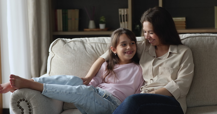 Lovely little girl her young caring mother having pleasant warm conversation seated on cozy sofa in modern living room at home. Trust, family bond, good relationships between parent and child concept | Shutterstock HD Video #1090949447
