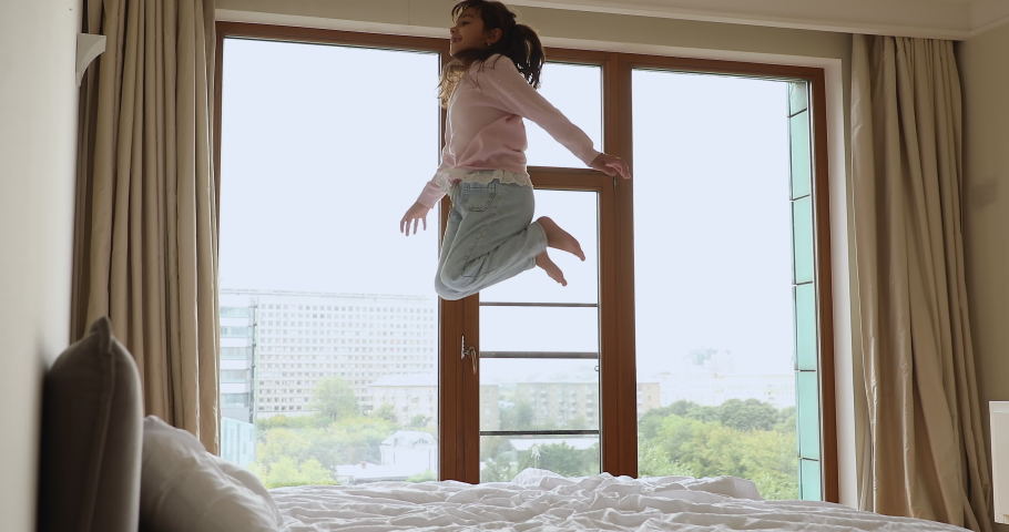 Little carefree girl jumps on bed in modern light bedroom, lovely kid pretend, imagining like fly in air, have fun alone indoor. Weekend leisure, hyperactive child, free time activity at home concept Royalty-Free Stock Footage #1090949461