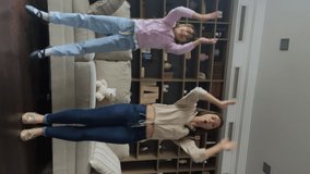 Happy mom and little cute daughter jumping, dance, move to favourite music looking at camera, vertical view. Record video for social network for vlog, active exercising at home with kid, hobby concept