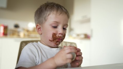 Child children eat sweet chocolate at table. Dirty face child mouth biting cocoa chocolate with teeth. Sweet breakfast of children at the table in kitchen. Happy kids with messy face eating chocolate