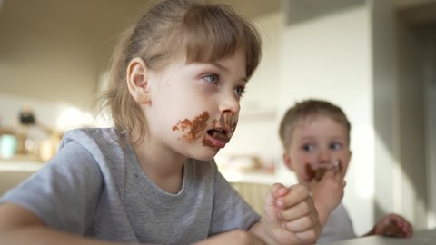 Boy and girl rides cocoa chocolate. Sweet breakfast at table in the kitchen. Dirty face of child. Happy family concept. Cheerful hungry children eat chocolate. Child eat chocolate sitting at table