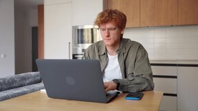 Focused young ginger irish man watching webinar video course on laptop writing note. Serious student looking at screen listening lecture study online on computer. E-learning, business training concept