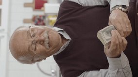 Happy old man very happy with his money.Winning the online lottery lottery. The old man is making a fan out of dollars.Video for the vertical story.