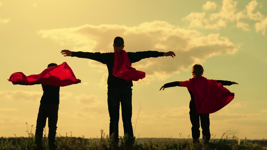 Happy kids playing superhero against sky. Boy plays superhero in red cape, childhood dream. Little hero in red cloak looks at sunset. Brave victorious child in raincoat plays, nature. Childhood dreams Royalty-Free Stock Footage #1090957521