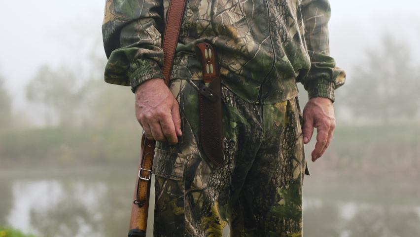 A hunter with a weapon slowly gets out of his knife near a misty lake