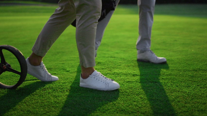 Two golfers legs walking on green grass field. Golf team carry sport equipment on course fairway close up. Unknown men going in sneakers sportswear uniform. Luxury lifestyle hobby recreation concept. Royalty-Free Stock Footage #1090958935