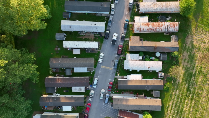 Top down aerial view of mobile homes. Drone follows road in between long row of houses. Low income housing in USA. Royalty-Free Stock Footage #1090962677