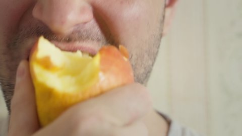 close-up man eats an apple, bites and chews. unshaven guy eating an apple. lower face eating fruit. not visible eyes mouth bites and chews a ripe apple, slow motion. use of vitamins and minerals food