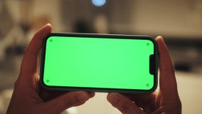 Woman using smartphone with chroma key at home. Young woman holding horizontal smartphone with green screen using streaming app watching video content in living room.
