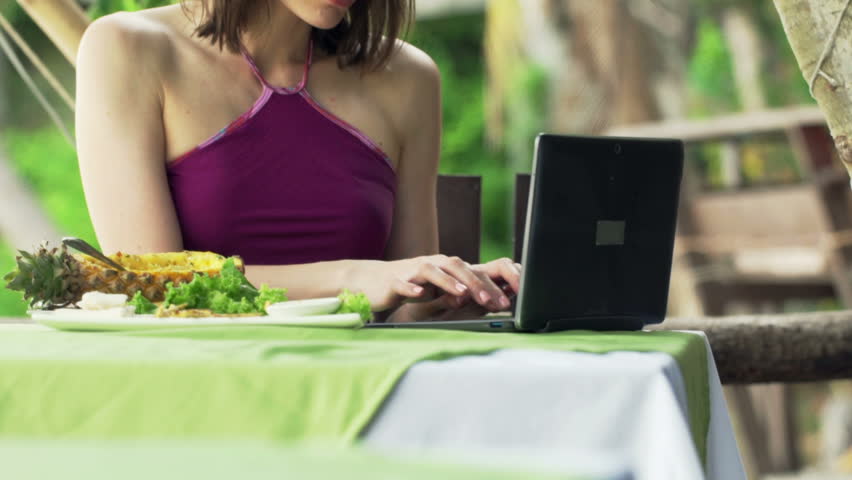 Woman hands using laptop and drinking juice sitting in exotic cafe 
