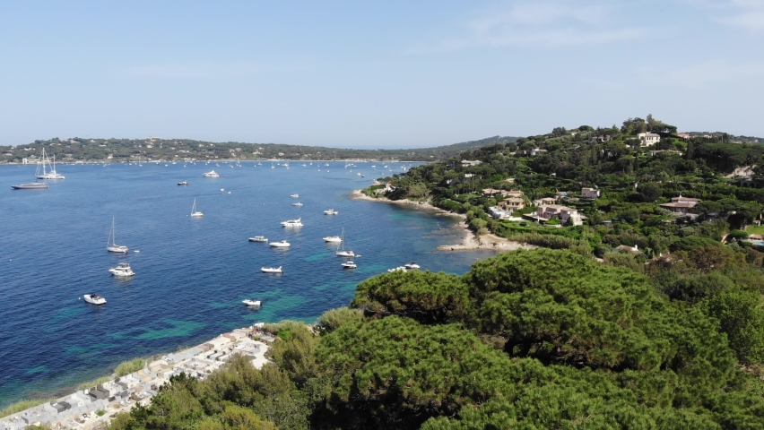Establishing shot flying over trees and revealing a beautiful mediterranean beach in Saint-Tropez, France