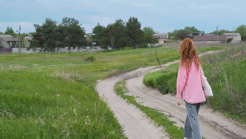 A young girl walks off into the distance along a country road. The girl goes into the sunset