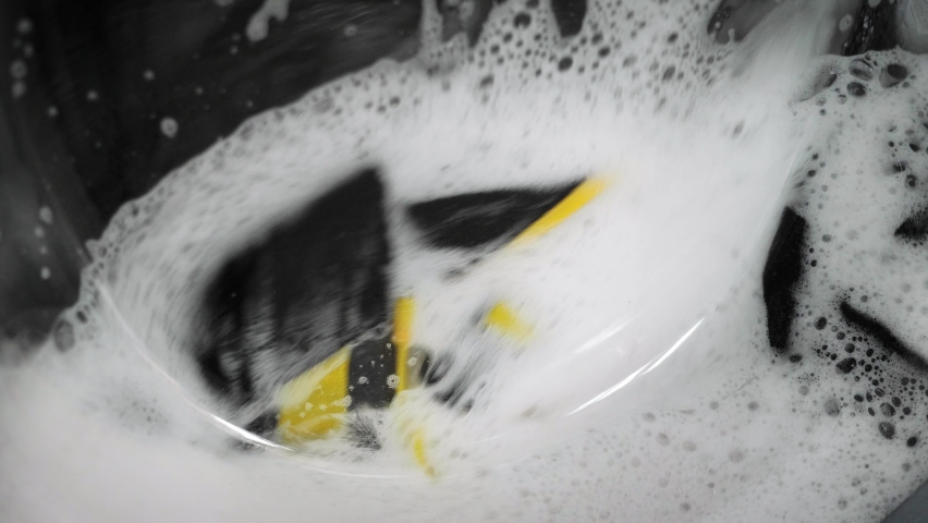 Washing machine, close up. Colorful laundry spinning in drum of washing machine with white soap bubbles.  | Shutterstock HD Video #1090972937