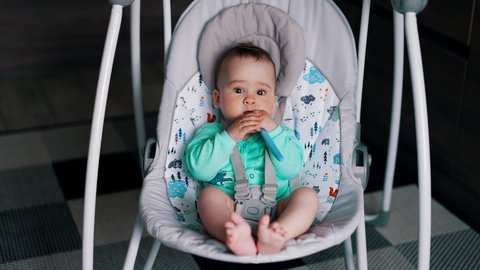 Lovely peaceful child sitting and rocking a in a baby chair. Toddler with dirty face and hands chewing spoon.