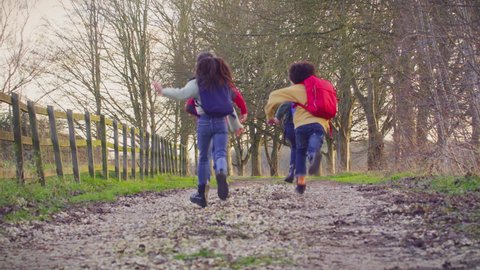 Children with school backpacks outdoors running away from camera along country lane - shot in slow motion
