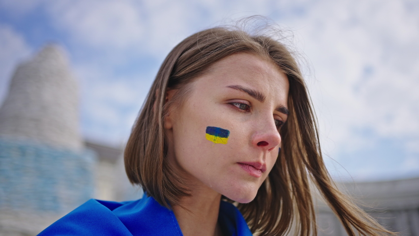 Ukrainian woman with paintings of national flag feels sorrow for native country crying on blurred background. Portrait of sad lady in center of Kyiv closeup Royalty-Free Stock Footage #1090986165