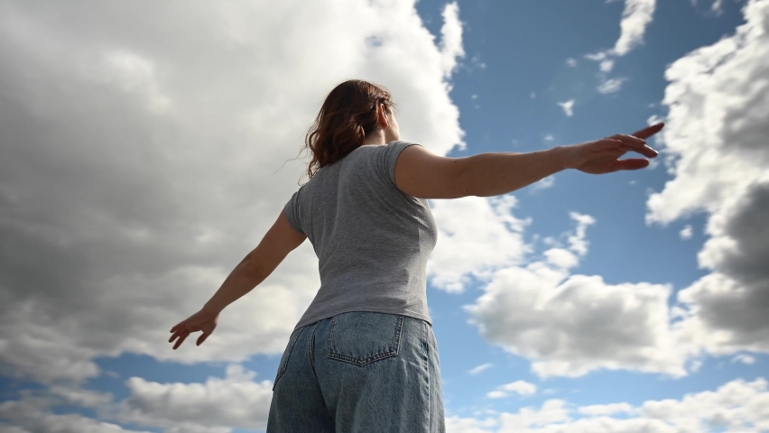Caucasian woman spread her arms like wings against a cloudy sky. Video 360 degrees.  Royalty-Free Stock Footage #1090988519