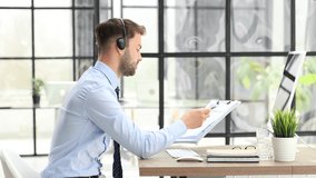 Smiling male call-center operator with headphones sitting at modern office, consulting online information, assistance to the client