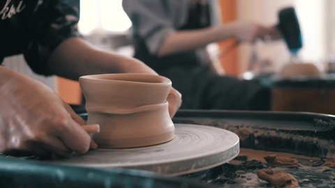 Master is cutting clay cup from potter's wheel, close-up in workshop. She is using wire, and moving ware by hand