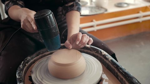 A woman dries a white clay product with a hair dryer on a potter's wheel. Craft, creativity, the process of working on a potter's wheel. High quality 4k footag