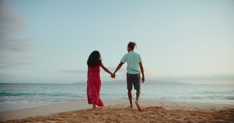 Beautiful aspirational young couple enjoying romantic sunset walk on the beach on vacation