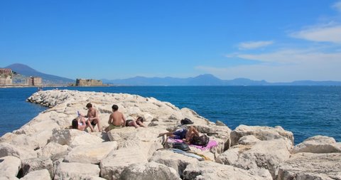 Naples , Italy - 06 01 2022: People Sunbathes At The Rocky Mediterranean Shore In Naples, Italy.