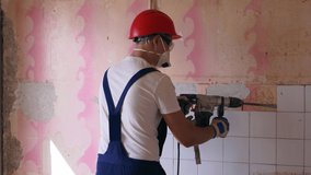 Contractor removes of ceramic tiles facing of the wall. Workman doing dismantling and demolition works with rotary hammer drill. Apartment renovation works. Builder in uniform and hardhat working. - Powered by Shutterstock - Get 15% off with code: PIKWIZARD15