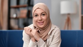 Muslim woman blogger in hijab, looking at camera, talking making video call, attractive popular arabic business vlogger recording vlog or webinar for channel, explaining, sitting at home on cozy sofa