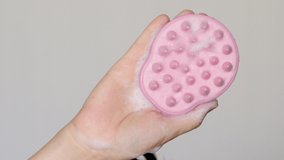 pink silicone brush with shampoo foam in woman, girl, hand. scalp massage. hair growth stimulating, hair care and beauty concept. home care. 4k close up video,raised up hand
