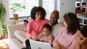 Happy multiracial family sitting on sofa and using laptop at home.