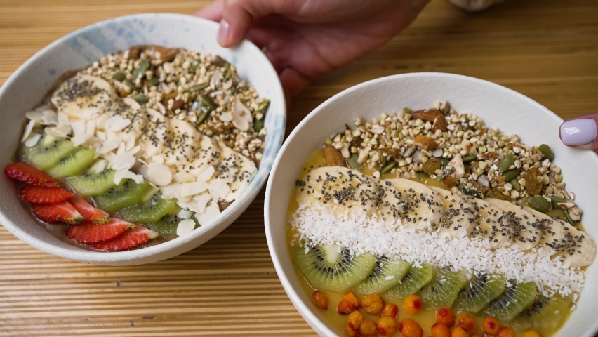Female hands put vegan bowls on table. Healthy fruit and cereals bowls enriched with vitamins for breakfast. Vegan bowls based on fruit puree closeup