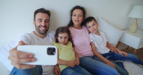 The older brother teases the younger sister during a video call. Young mom hugs her spoiled children while father talks on video call. Video footage, 4 K