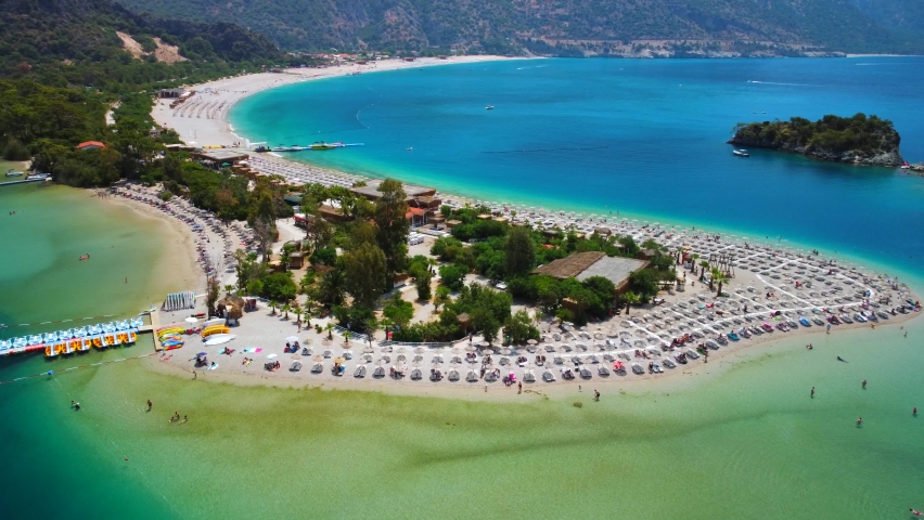 Amazing aerial view of Oludeniz peninsula in Fethiye, blue lagoon, drone flight over sandy beach, turquoise sea, beach resort with sun beds and umbrellas, hot summer day. Royalty-Free Stock Footage #1091012425