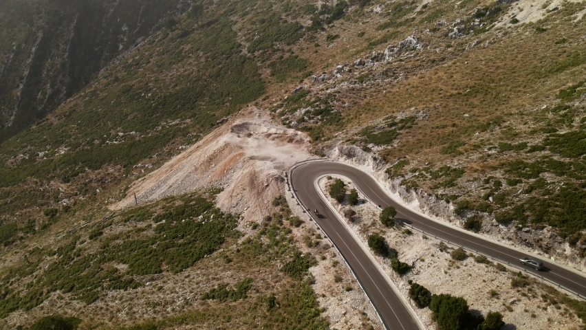 Drone following motorcycle driving along winding road in Llogara mountain valley, Albania. Aerial view of Balkan landscapes. Concept of freedom and adventure