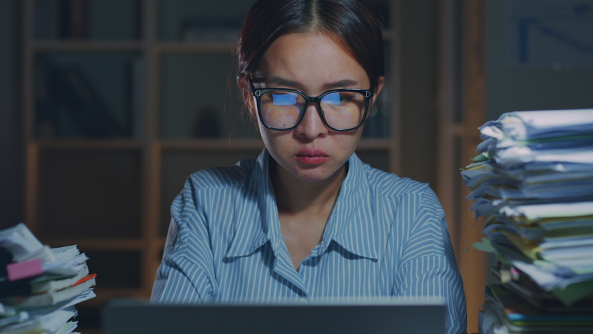 Overworked young Asian office employee wearing eyeglasses yawn during working on laptop computer overtime at night in office  Royalty-Free Stock Footage #1091014889