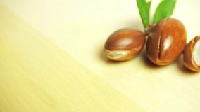 Argan nuts with green leaves motion on wooden background. 