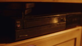 Close Up of a Person Inserting a VHS Cassette in a Player with Nostalgic Vacation Footage from Home Video Camera. Retro Nineties Technology Concept. Old VCR Shot with Shallow Depth of Field and Bokeh.