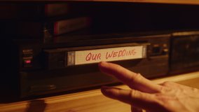 Close Up of a Person Inserting a VHS Cassette in a Player with Nostalgic Wedding Footage from Home Video Camera. Retro Nineties Technology Concept. Old VCR Shot with Shallow Depth of Field and Bokeh.
