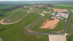 AERIAL: View of racing circuit and facilities with sport race cars training laps. Racing cars moving in clockwise direction of tarmac racecourse ring. Adrenaline motor sport for high-speed enthusiasts