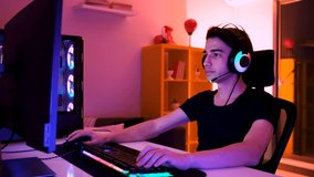 Gamer playing and winning in online video game, excited happy gamer playing and winning on his personal computer. His room and pc have warm neon lights. He is having a fun evening at home.