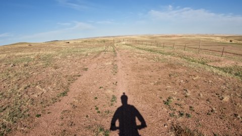First person POV with cyclist shadow from riding a fat mountain bike on a trail in Colorado prairie and arriving to a gate, early spring scenery in Soapstone Prairie Natural Area